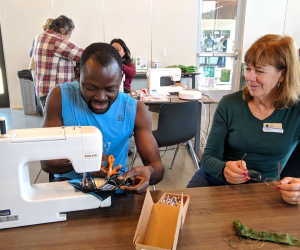 Fixit Clinic volunteer helps participant use sewing machine to make a repair
